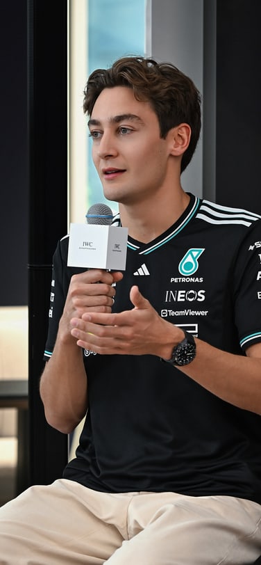 ブランドのロゴ入りのブラックユニフォームとIWCの時計を身に着けた、IWCブランドアンバサダーのF1グランプリ優勝者ジョージ・ラッセル。