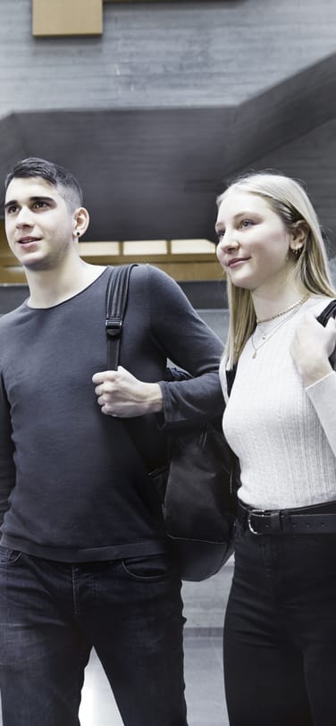 Two smiling young people with backpacks inside IWC building