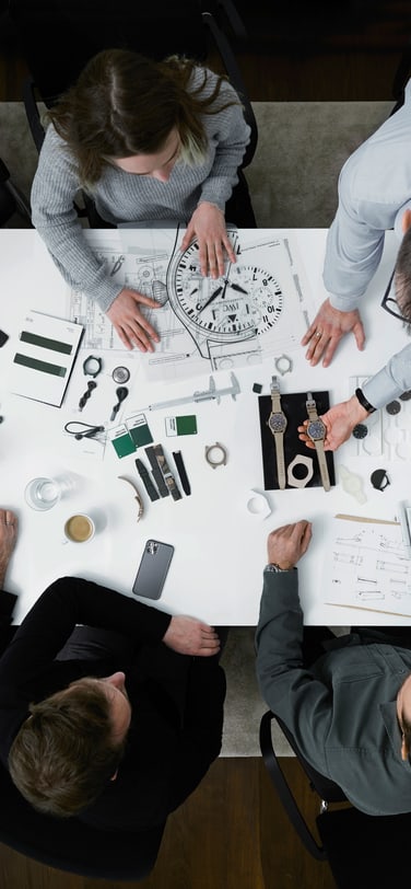 Five people sitting around a table discussing watches and sketches