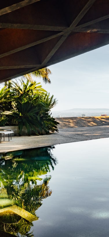 A luxurious outdoor scene at the Goldstein Residence in Los Angeles, featuring a modernist concrete structure, a tranquil swimming pool, and tropical landscaping under a clear sky