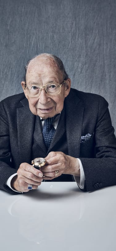 Elder gentleman in a gray suit holding a perpetual calendar wristwatch