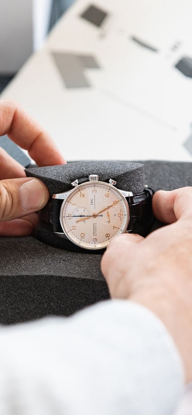 an IWC watch with white dial and black strap is placed on a holder by two male hands