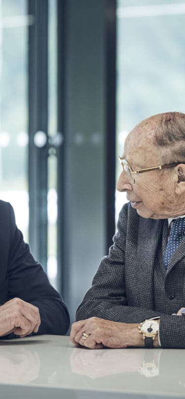 Two watchmakers in suits sitting next to each other in conversation