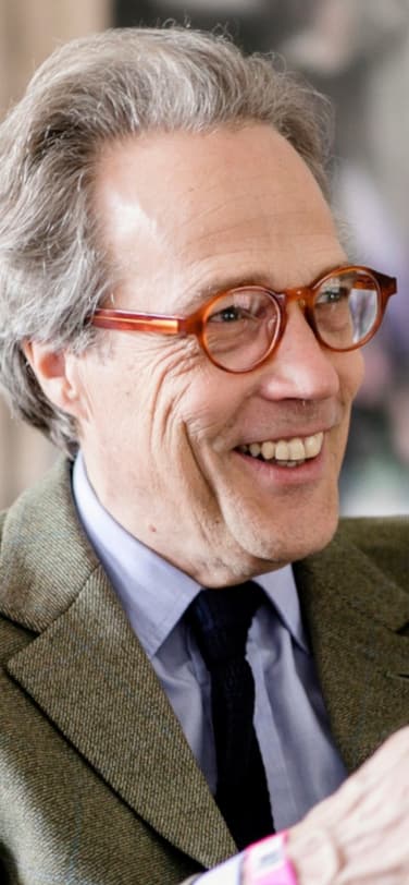 El undécimo duque de Richmond, luciendo gafas rojas y chaqueta verde, sentado y sonriendo mientras habla en un evento.