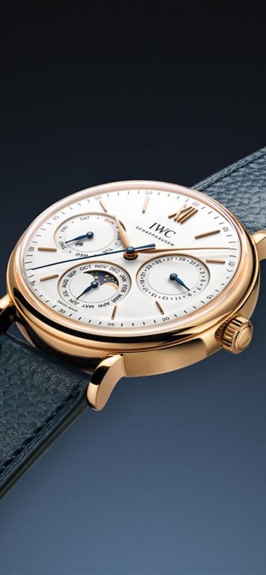 IWC Portofino watch with white dial, gold case and blue strap on a dark blue background