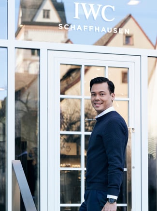 A man standing in front of a building door with IWC Schaffhausen writing on it