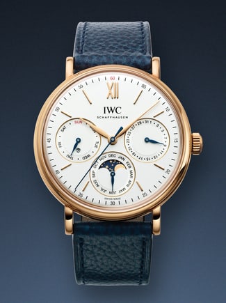 IWC Portofino watch with white dial, gold case and blue strap on a dark blue background