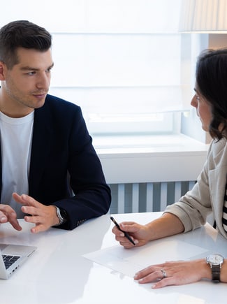 A man in a suit and a woman in a striped shirt sit around the table