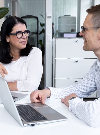 A woman and a man sitting at a table with laptops open