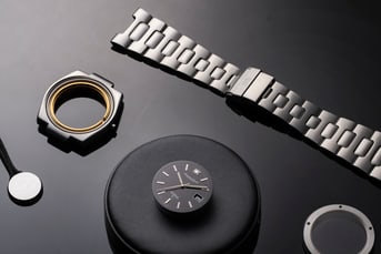 Disassembled IWC Schaffhausen watch components arranged on a black surface, showcasing the bracelet, case, dial, and case back.
