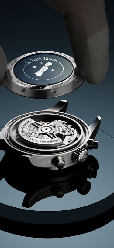 Close-up of a mechanical wristwatch being assembled, with gloved hands lifting the case back above the exposed movement. The watch sits on a reflective surface, showing intricate internal gears and components in detail.