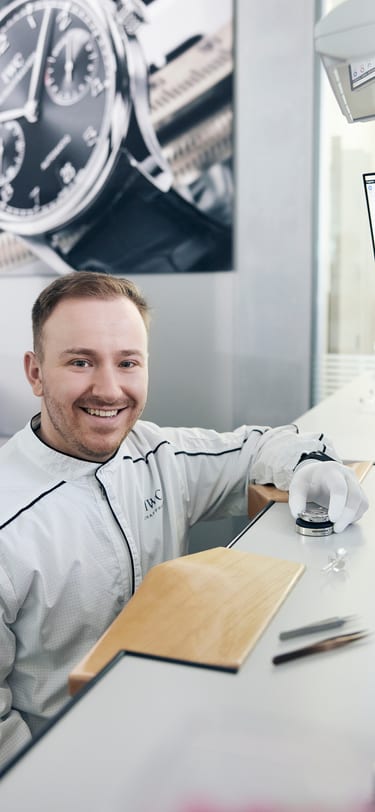 A wachmaker holding a watch movement smiling into the camera