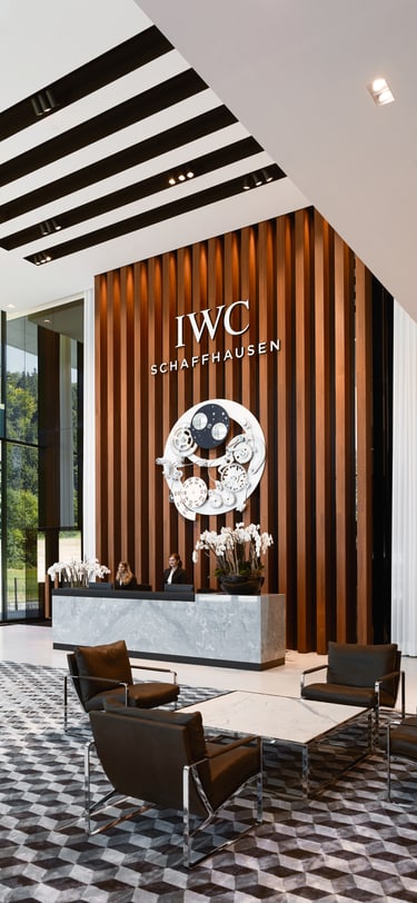 image showing the lobby of IWC Manufakturzentrum building, with brown interior walls, reception desk and two female receptionists standing behind it
