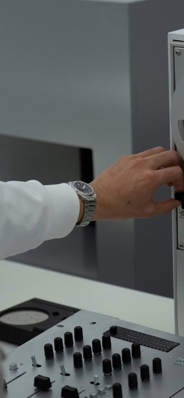 A person wearing headphones and an IWC watch operates a vintage reel-to-reel tape recorder in a recording studio