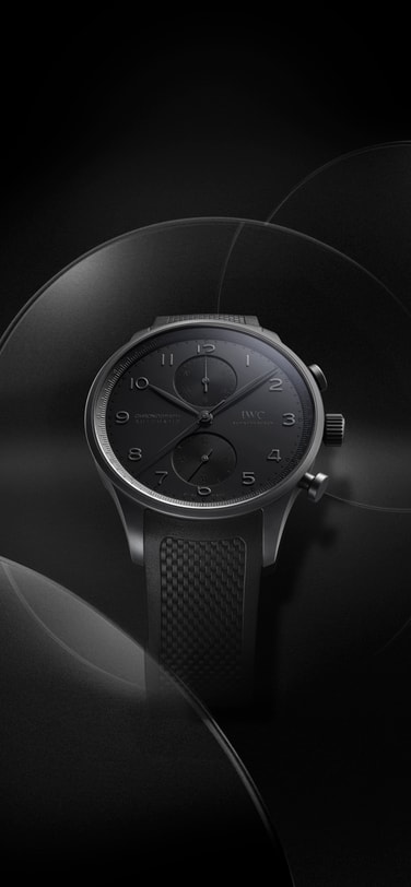 IWC Portugieser Chronograph Ceratanium® on a black background; black dial with subtle reliefs and patterned black rubber strap.