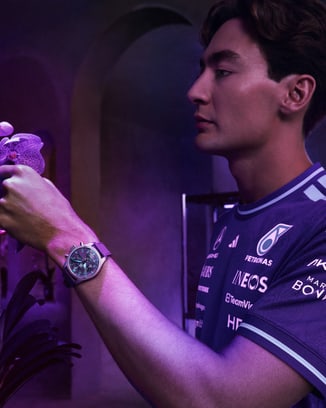 George Russell looking at a purple orchid, wearing Petronas team shirt modelling Pilot's Watch Chronograph 41 Mercedes-AMG Petronas Formula One™ Team
