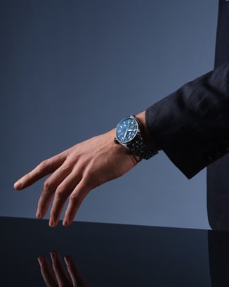 Studio shot of a person in a dark suit with their arm extended on a reflective surface, wearing an IWC watch