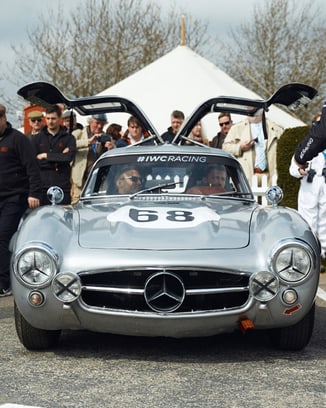 A silver Mercedes-Benz SL 300 “Gullwing” with open doors standing near the race track at Goodwood.