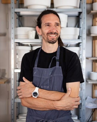 Ceramicist Laurin Schaub wearing a black t-shirt and white ceramic watch standing in front of his pottery artifacts