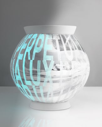 White ceramic moon jar with "LUX PERPETUA" text, partially glowing blue