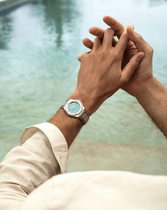 Close-up of a man's wrist wearing an IWC watch with a mint turquoise dial by the pool.