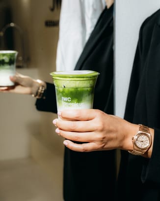 Close-up of a wrist wearing an IWC Ingenieur Automatic 35 gold watch, holding an IWC-branded matcha drink