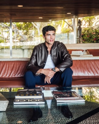 Male model dressed in a black leather jacket and seated on a rust-red leather couch sporting an Ingenieur sports watch in green ceramic