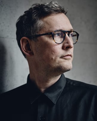 Portrait image of a man wearing glasses in front of a grey background