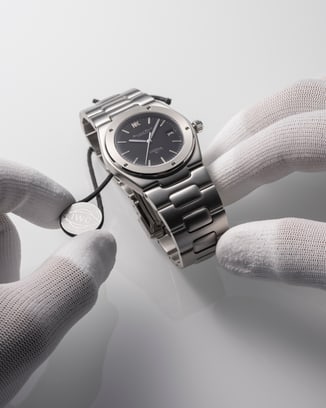 Hands in white gloves holding the Ingenieur SL watch with IWC.Curated. certification badge.